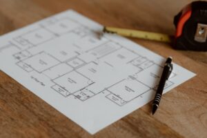 A detailed architectural blueprint on a wooden desk with a tape measure and pen.